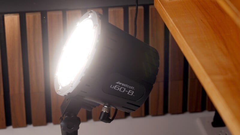 A bright studio light labeled "Westcott u60-B" is mounted on a stand, angled towards a wooden surface. The background features wooden acoustic panels.