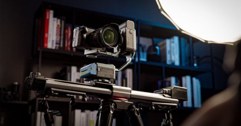 A camera mounted on a motorized slider with a stabilizer, set up indoors. The background features a bookshelf filled with books, and a bright studio light illuminating the setup.