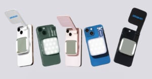 Five smartphones in different colors (white, green, pink, blue, and black) with foldable LED lights labeled "amaran" attached to the back. Each phone has a square LED panel and a flip-up cover, set against a gray background.