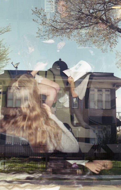 A double exposure image showing a group of people sitting and reading outdoors, superimposed over a residential house with a fenced yard. The scene captures a blend of leisure and suburban architecture under a partly cloudy sky.