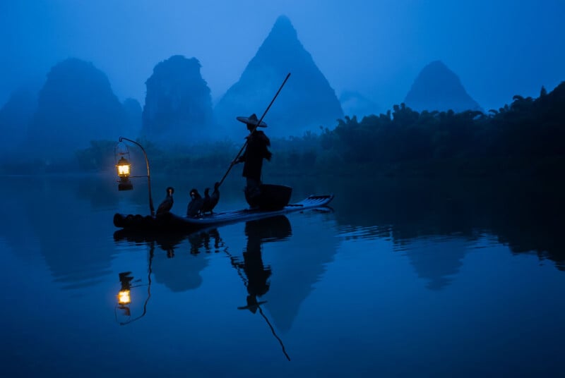 A fisherman stands on ⁣a bamboo raft on a calm river at dusk. He holds a pole ⁤and⁤ is accompanied by‍ cormorants. A lantern hangs from the raft, casting a warm glow. misty karst mountains rise in⁣ the background, creating a serene and ‍mysterious atmosphere.