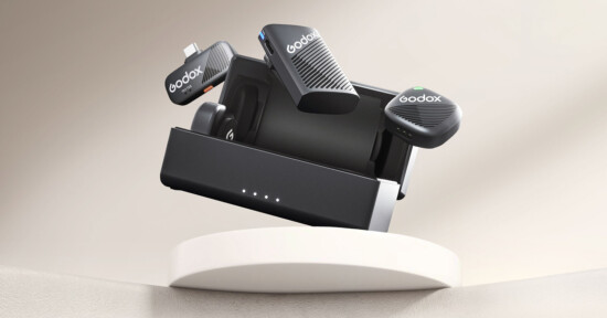 A Godox wireless microphone system with a charging case showcased on a round white platform. The microphones and case feature sleek black designs with the Godox logo. The background is a soft gradient of light beige tones.