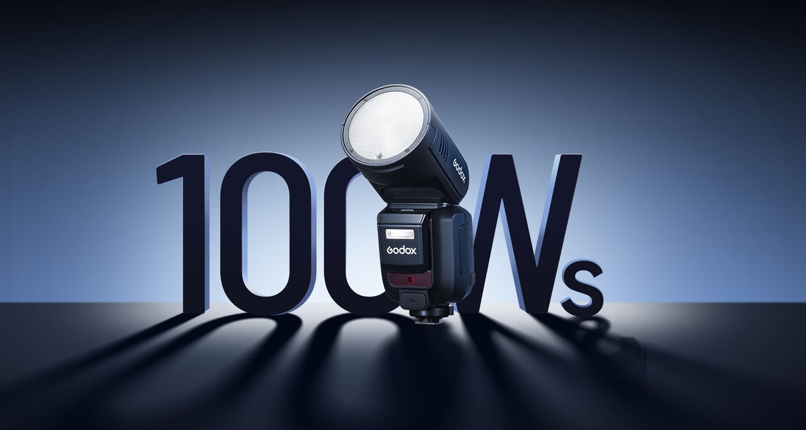 A Godox camera flash with a round head stands in front of large, bold numbers "100Ws" against a gradient blue background. The flash casts a shadow on the surface, creating a dynamic composition highlighting the flash's power.