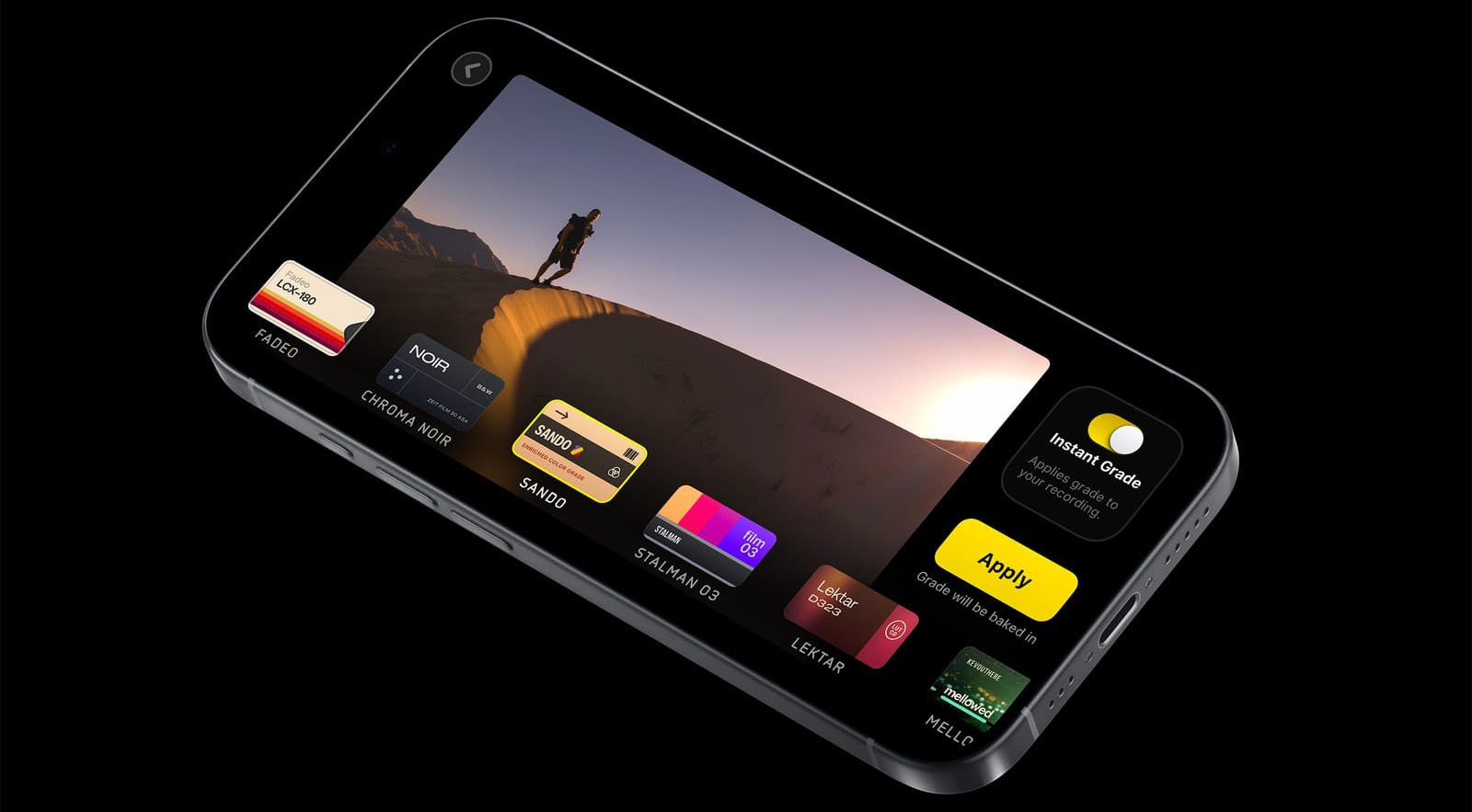 A smartphone displaying a photo editing app interface. The screen shows various filter options and a person standing on a sand dune. The app includes buttons labeled "Apply" and "Instant Grade." The phone is tilted on a dark background.