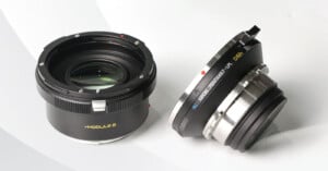 Two camera lenses are pictured against a light background. One lens lies flat showing the glass element, while the other is tilted, displaying the text "KERLEE IBERIT 33mm F0.9." The lenses have a sleek black and silver design.