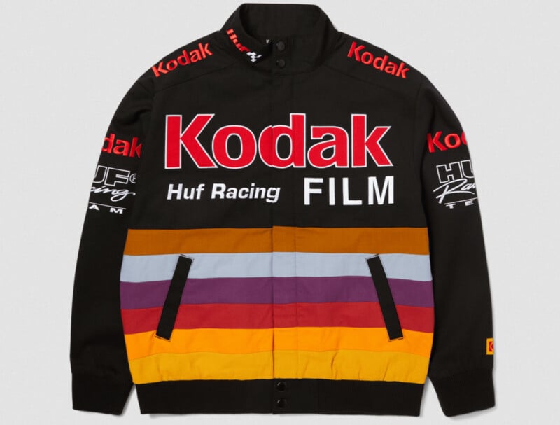 A black jacket with vibrant red "Kodak" text across the chest, accompanied by "Huf Racing" and "FILM" logos. It features colorful horizontal stripes in purple, orange, and yellow across the bottom half, with additional text on the sleeves and shoulders.