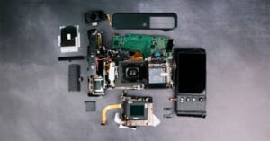 A disassembled camera is laid out on a dark surface, showcasing various components including the lens, circuit board, and outer casing. The parts are neatly arranged, highlighting the intricate inner workings of the device.