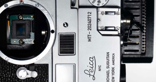 Close-up of a disassembled Leica camera showing its internal components, including the autofocus sensor and lens mount. Model number MT-20240712 is visible on the metal body, along with engravings "Michael Suguitan" and "New York America.