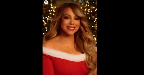 A person wearing a red dress with white trim, smiling in front of a background decorated with Christmas lights.
