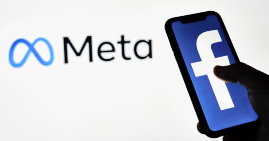 A silhouette of a hand holds a smartphone displaying the Facebook logo. In the background, the Meta logo and name are visible, symbolizing the company's rebranding.