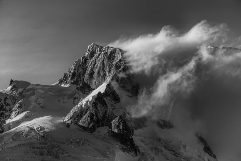 A dramatic black ‍and white photograph ⁣of a rugged, snow-covered mountain peak partially obscured by ⁤swirling clouds. The​ scene captures a sense of majesty and mystery.