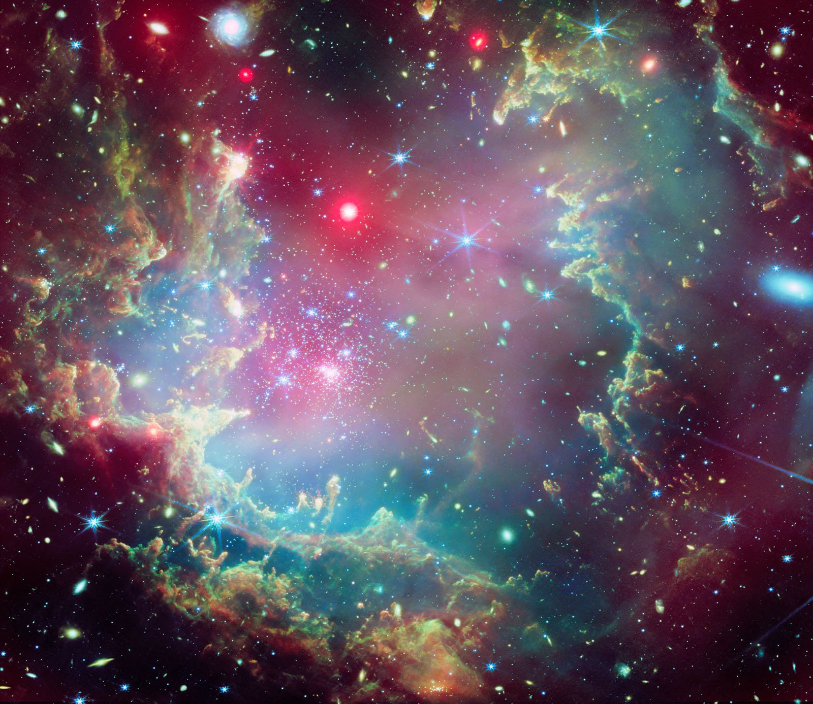 A vibrant cosmic scene showing swirling clouds of gas and dust in pink, green, and blue hues, dotted with sparkling stars of various colors, set against the dark backdrop of space.