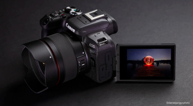 A Canon EOS R10 camera with an articulated screen displays an image of a glowing orb over water against a dark background. The camera is positioned on a black surface.