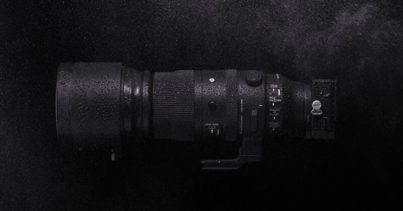 Black telephoto camera lens with water droplets on its surface on a dark and foggy background.