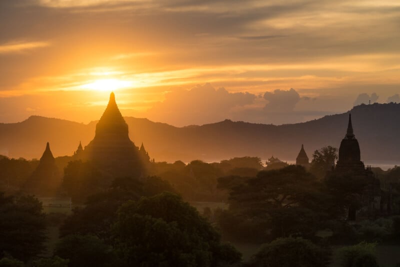 A breathtaking sunset over an ancient temple landscape, silhouetting​ the pagodas against a golden sky. ⁢Dense ​greenery 