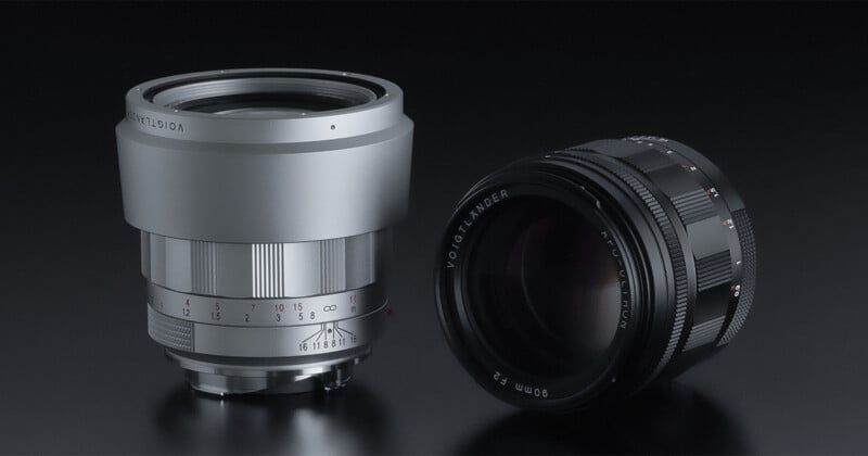 Two camera lenses on a dark surface. The left lens is silver with red and black markings, while the right lens is black with white text. Both lenses have metallic finishes and are positioned side by side.