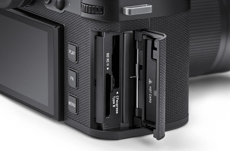 Close-up of a camera with an open memory card slot. Visible are slots for an SD card and CFexpress Type B card. The camera body features buttons labeled Play, Fn, and Menu, along with textured grip detailing.