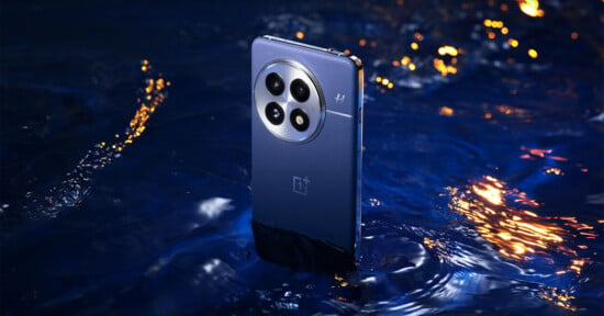 A smartphone partially submerged in water, displaying its rear camera setup with four lenses and a branded logo. The background features rippling water with reflections of orange and yellow lights, creating a vibrant contrast.