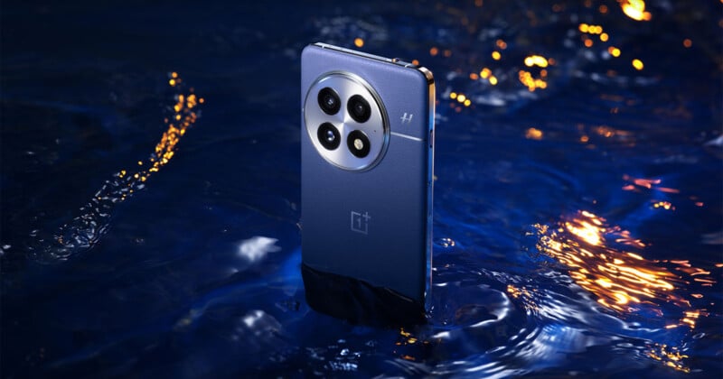 A smartphone partially immersed in water, showcasing its rear camera arrangement with four lenses and a branded logo. The backdrop features shimmering water with reflections of orange and yellow lights, creating a lively contrast.