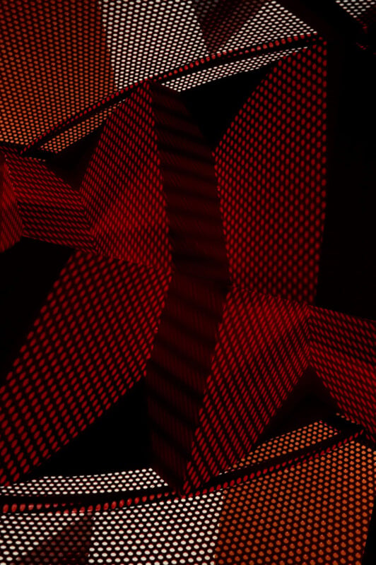 An abstract composition featuring red and orange geometrical forms adorned with dot patterns. The arrangement incorporates overlapping triangular shapes, creating an impression of depth and contrast against a dark backdrop.