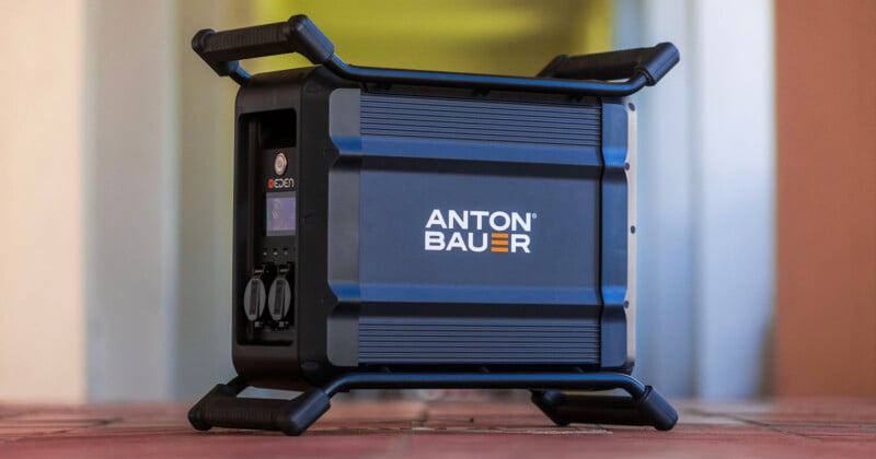 Portable power station labeled "Anton Bauer" in blue with black protective frame and handles, shown on a tiled floor indoors.