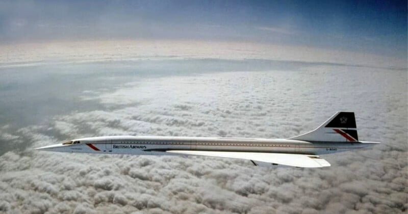 A British Airways Concorde jet flies above a blanket of clouds. The sleek, white, supersonic aircraft features a distinctive elongated nose and delta wings, set against a horizon blending sky and clouds.