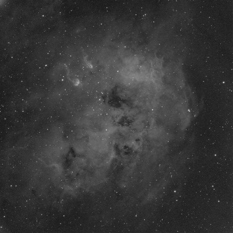 Grayscale image of a star-filled nebula with cloudy, diffuse shapes and varying intensities of light. Stars are scattered throughout, creating a celestial scene against the darker space backdrop.