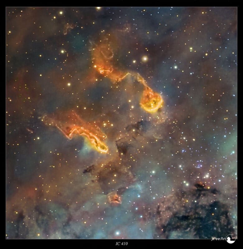 Colorful cosmic scene of IC 410, featuring wispy, bright orange and yellow clouds set against a backdrop of star-filled space with shades of blue and purple. Some clouds appear as distinct, elongated shapes.