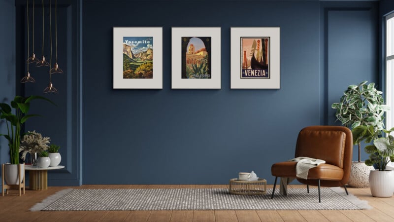 A stylish room with three framed travel posters on a dark blue wall. Below, a brown leather chair sits on a gray rug, accompanied by a small side table. A potted plant is in the corner, and several pendant lights hang from the ceiling.