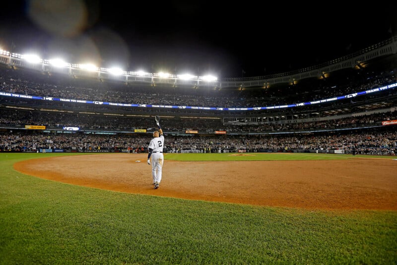 A baseball player in a white uniform stands on the field waving to a large, illuminated stadium crowd at night. The scene captures the atmosphere of a significant game or event.