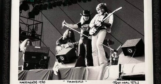 Black and white photo of a rock band performing on stage. Three guitarists are playing, with one wearing a hat. A prominent "Freebird" caption is visible. Concert lights and speakers can be seen in the background.