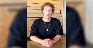 Mark Zuckerberg sits at a table, wearing a black shirt and a gold necklace. The background features wooden panels and a white wall strip.