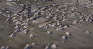 Aerial view of a lunar surface with numerous craters and uneven terrain. Shadows accentuate the depth of the craters, and the surface appears rocky and desolate, showcasing the texture of the moon's landscape.