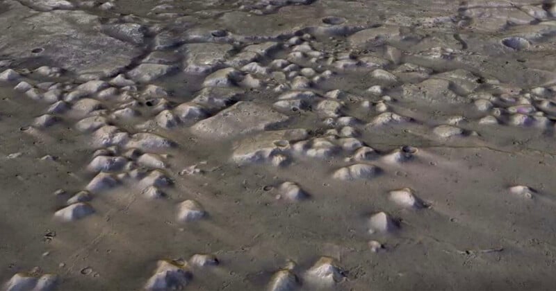 Aerial view of a lunar surface with numerous craters and uneven terrain. Shadows accentuate the depth of the craters, and the surface appears rocky and desolate, showcasing the texture of the moon's landscape.