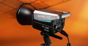 A Nanlite FC-120C studio light on a stand, positioned against an orange gradient background. The light features a control panel and a handle, showcasing its design and functionality.