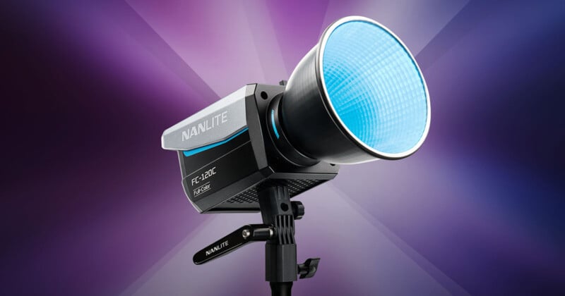 A Nanlite FC-300B studio light with a black finish and blue light diffusion sits against a purple gradient background. The light is mounted on a stand and features a reflective dish.