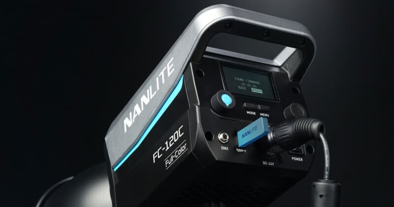 Close-up of a Nanlite FC-120C professional studio light against a dark background. The display screen shows settings, and various controls are visible. A cable is connected to the right side of the device.