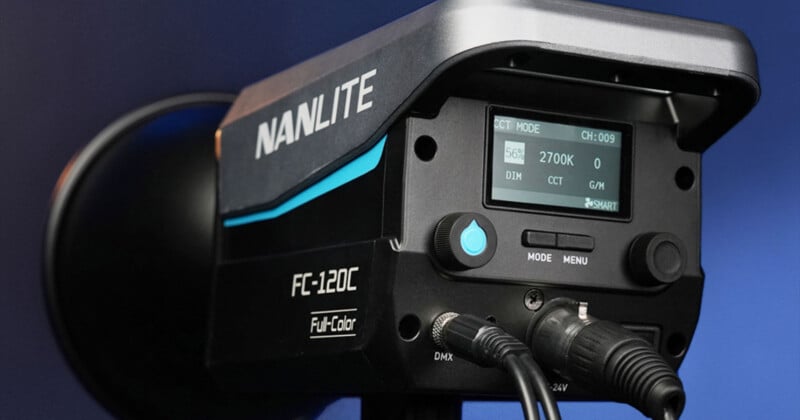 Close-up of a Nanlite FC-120C full-color LED light panel with digital display showing settings. The panel's controls and connectors are visible, set against a dark blue background.