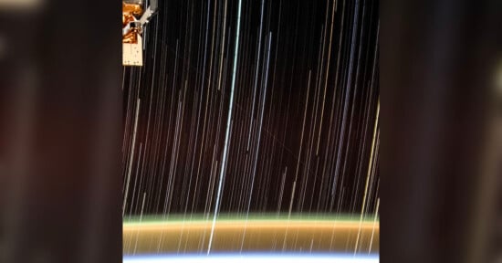 A long-exposure photo taken from the International Space Station showing bright star trails streaking across the dark sky, with a curved, illuminated edge of the Earth visible at the bottom.