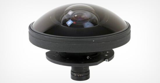 A dome-shaped 360-degree camera lens with a transparent cover on top, mounted on a black circular base and cylindrical support underneath, set against a plain white background.