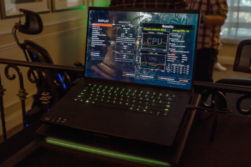 A laptop with a backlit keyboard is displaying a performance monitoring program with graphs and statistics related to CPU usage and graphics settings. The screen shows data about a gaming application's performance.