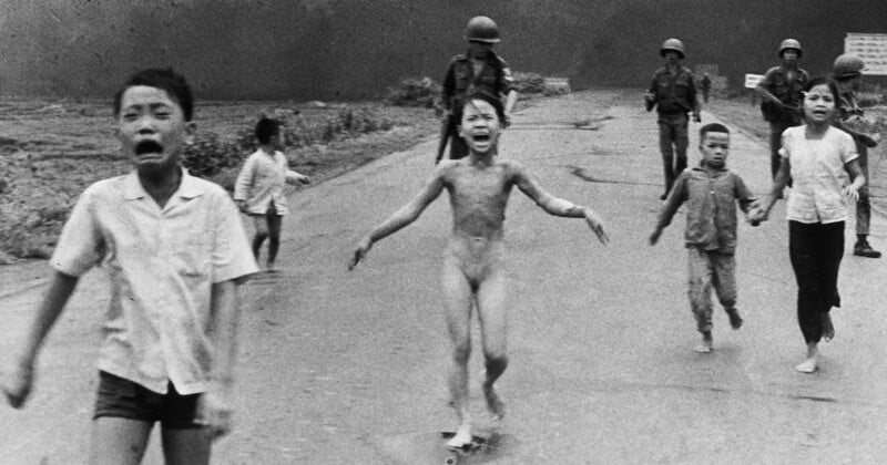Children run down a road, appearing distressed, with soldiers walking behind them. A central child, without clothing, is crying. The background is a dark smoke-filled sky, conveying a sense of urgency and fear.