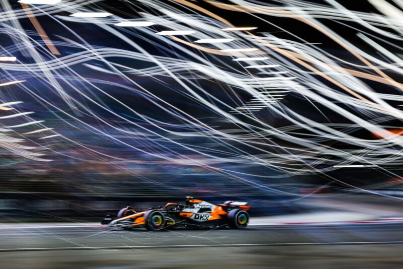 A Formula 1 car speeds through a racetrack at night. Streaks of light trails across the image create a dynamic sense of motion, highlighting the car's fast pace. The lights blur into the dark background, emphasizing speed and excitement.