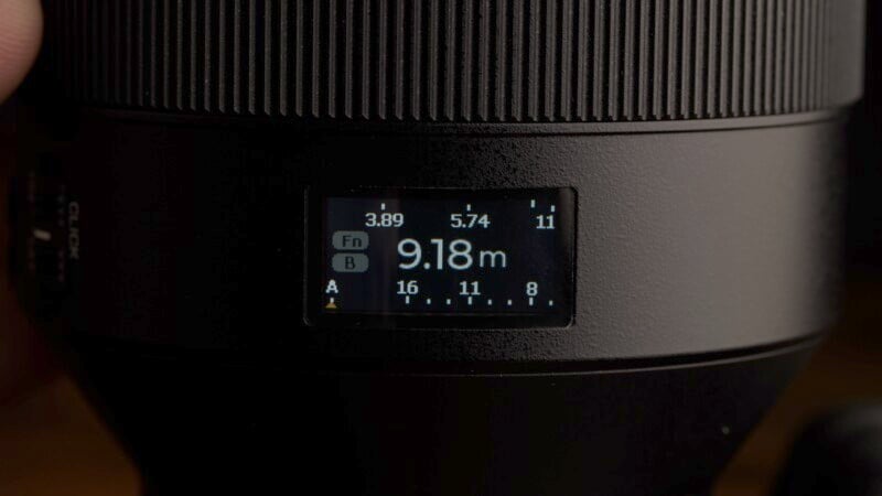 Close-up of a camera lens with a digital display showing a distance of 9.18 meters, aperture settings ranging from 3.89 to 11, and function options labeled "Fn" and buttons "A" and "B.