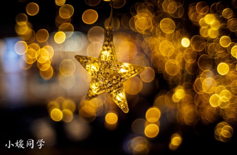 A glowing star-shaped ornament is hanging against a background of golden bokeh lights. The bokeh effect creates a warm, festive atmosphere. Chinese characters are visible in the bottom left corner.