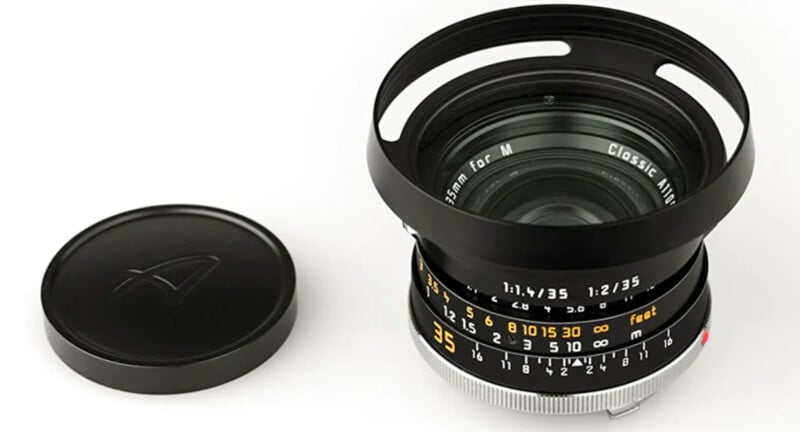 A black camera lens with detailed markings and a silver focusing ring is placed next to its lens cap on a white background. The lens has a prominent hood attached.