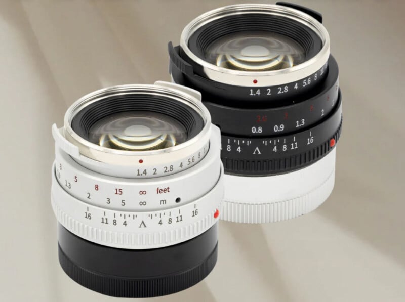 Two camera lenses are positioned side by side on a reflective surface. The lens on the left is silver with engraved markings, while the one on the right is black. Both have detailed aperture and focus scales visible.