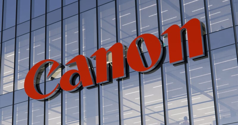 The image shows a glass building facade with a large red "Canon" logo prominently displayed. The reflective windows capture the sky and surrounding lights.