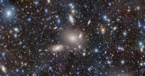 A vast, colorful galaxy cluster filled with numerous bright stars and galaxies against a dark backdrop. The image showcases a celestial spectacle with scattered light sources of varying sizes and colors, highlighting the universe's vastness.