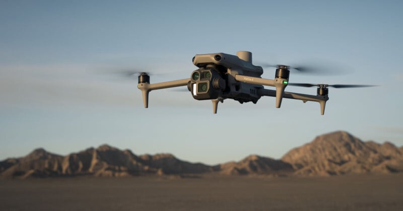 A drone flying in a desert landscape with four propellers and a camera attached, set against a backdrop of distant mountains under a clear sky.